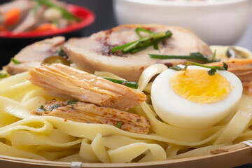 Noodles with pieces of meat and an egg in a bamboo plate on a dark table. Asian food concept. Close-up