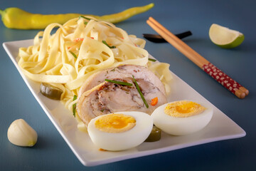Noodles with pieces of meat and eggs in a white plate and dim sum with various traditional mushroom, soy and vegetable appetizers with chopsticks on a blue table. Asian food concept