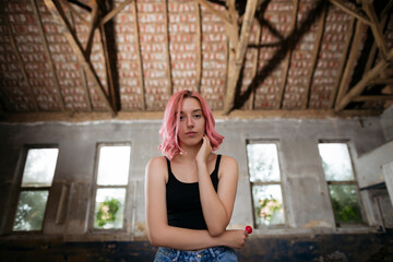 Young funky teenage girl with pink hair holding lollipop candy in abandoned building.