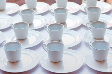 Many white cups of tea on the table in the Restaurant, Hotel. Many empty tea cups. white tea mugs and saucers lined up in rows on the table.