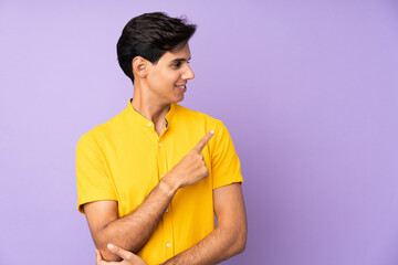 Man over isolated purple background pointing to the side to present a product