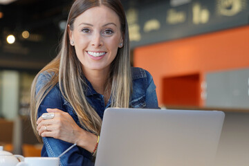 Young woman sitting at coffee shop and working on laptop