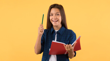 Teenage girl holding notebook and raising pen up at studio