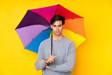 Man holding an umbrella over isolated yellow background keeping arms crossed