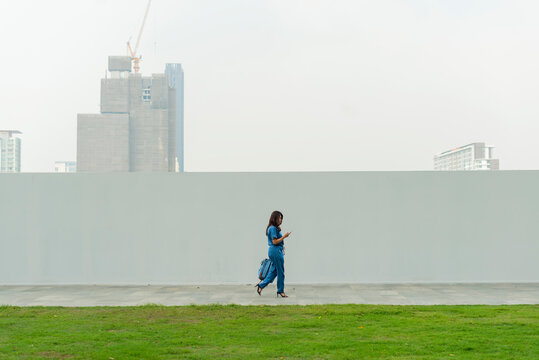 Asian Woman Walking Outdoors And Using A Smartphone On A City Street And Street Wall Background ,Building In City Background.