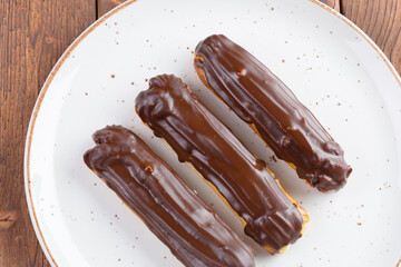 Chocolate eclairs on white plate on wooden table