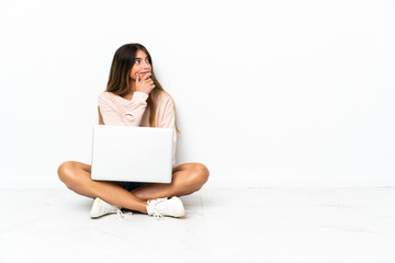 Young woman with a laptop sitting on the floor isolated on white background having doubts and with...