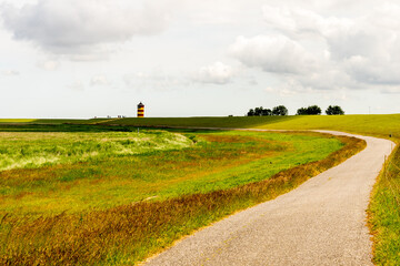 view on Pilsum lighthouse in the landscape of East Frisia with tourists walking around the dike and taking photographs
