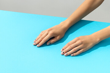 Womans hands with nude nail design over blue background