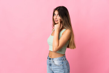 Young caucasian woman isolated on pink background showing something
