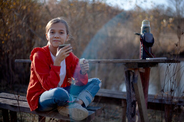 Preteen girl  holding thermos  and pours tea in the nature