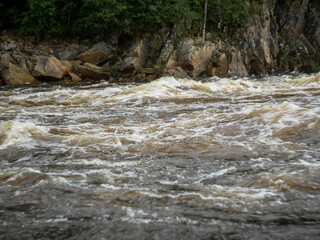 big waves on the rolling threshold of a mountain river against the background of rocks and forests