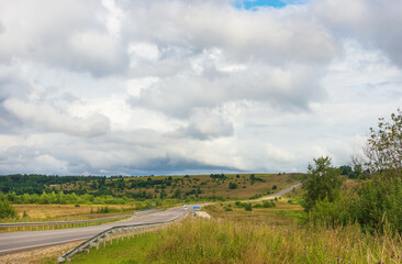 Paved, winding road in the countryside, in Russia, among fields and forests, on a hill. Concept of summer vacation at home.