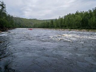 Rifts and rapids on a mountain river against the background of mountains and forests in summer swimming facility in the distance