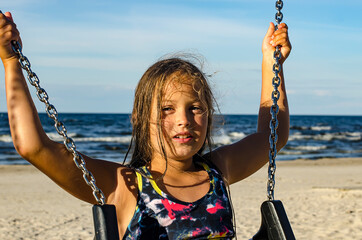 Cute girl 8-9 years old on swing against background of sea.