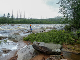 a boy with a paddle in a helmet with a life jacket standing on a large rock near a mountain river