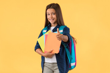 Smiling schoolgirl showing thumb up at studio