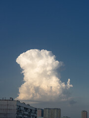 Single cumulus cloud over cityscape against blue sky. Solitary white huge cloud looks like tower over roofs of the apartment buildings at clear sky.