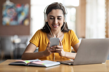 Young girl student sitting at cafe, using laptop and smartphone