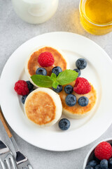Syrniki, cottage cheese fritters with berries and honey on a plate. Healthy breakfast or dessert. Cheesecakes