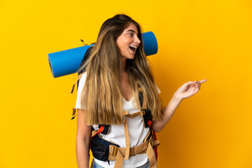 Young mountaineer woman with a big backpack isolated on yellow background pointing finger to the side