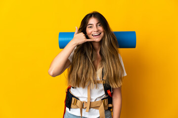 Young mountaineer woman with a big backpack isolated on yellow background making phone gesture. Call me back sign