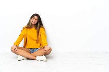Young woman sitting on the floor isolated on white background with arms crossed and looking forward