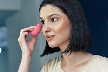 Makeup artist girl applying foundation on her skin during her tutorial online. Pretty young brunette woman making herself make-up.