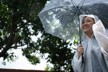 Asian women smiling and wearing a raincoat on a rainy day. She used her hand to cover her head with a hat.