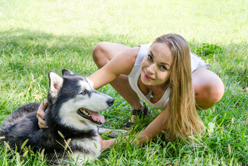 young beautiful girl hugs a husky and posing at the camera in the park.