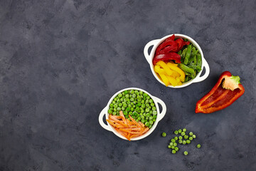 Frozen vegetables:  string beans, pepper, green peas and carrot in bowls on a  dark grey background. Top view with copy space.