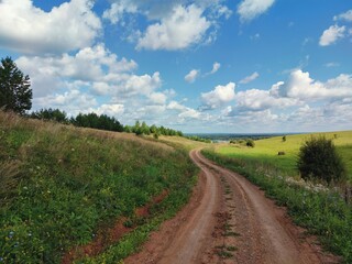 winding road through a hilly field against a blue sky with clouds on a sunny day