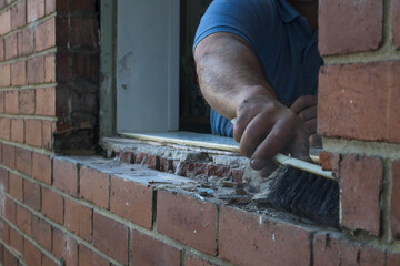 Hand brush being used to clean hole in wall after window frame has been removed by workman