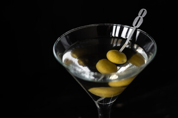 Classic Martini cocktail with two green olives in metal stick. Close up shot with dark background.