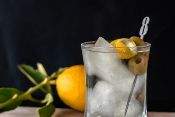 Iced Martini cocktail in glass with two green olives in metal stick and lemon garnish. Close up shot with lemons in the background.