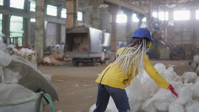 Waste processing plant. Technological process. Recycling and storage of waste for further disposal. Woman worker in hard hat gathering, pressing used plastic tape on recycle factory