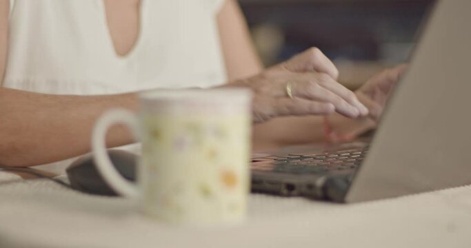 Woman Types On Her Laptop Behind A Blurred Mug At Home
