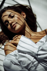 A woman in a white dress lies on the floor. White studio floor background. Natural makeup.
