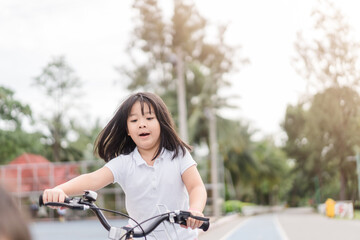 Fototapeta na wymiar 6 years old happy Little asian girl child learn to ride bicycle at park.she ride bicycle to School first day :Healthy happy young adorable lovely female kid.Back to school.family activities outdoor.