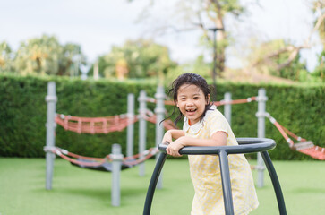 Asian kid girl playing on a swing and having fun in park.Little asian girl climbing rope at playground.Asian child girl playing on playground in outdoor park.Happy Little asian girl outdoor play park.