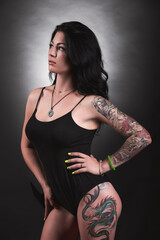 Tattooed brunette in black swimsuit on black background