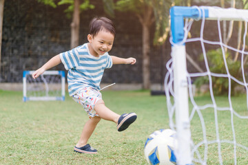 Asian toddler boy playing soccer or football in football field park outdoor.3 years old asian boy kicking football on the grass field.Little Boy Shooting at Goal, Winner, Sport activity in sport club. © MIA Studio