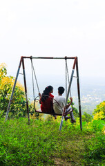 Romantic couple swinging on swings over the green mountain landscape with sky. Freedom concept. Touristic place. Khagrachhari, Bangladesh/ 2020.