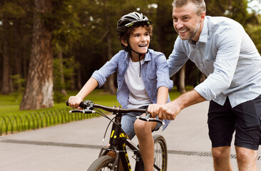 Obraz premium Boy learning to ride a bicycle with his adult father
