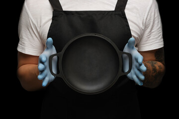 A man in an apron holds an empty frying pan. Mockup.