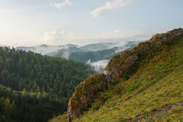Mountain landscape. Close-up rock. Fog on the mountain slopes. Green grass and trees.