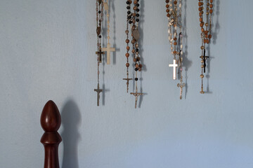 Different rosaries hanging on blue wall by bed and copy space. Rosary collection exposed at home...