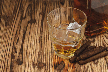 Glass of whiskey and rolled cigars on wooden table