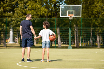 Obraz premium Man posing with little boy on basketball pitch back view