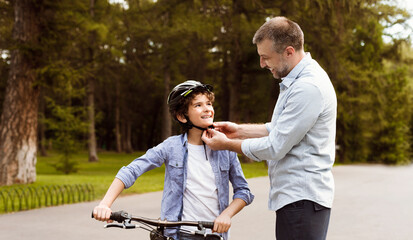Handsome man putting protective helmet on curly boy